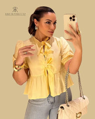 Mujer vistiendo la Blusa Matilda Amarilla con diseño peplum, mangas abullonadas y lazos frontales, combinada con jeans para un look casual y moderno