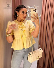 Mujer vistiendo la Blusa Matilda Amarilla con diseño peplum, mangas abullonadas y lazos frontales, combinada con jeans para un look casual y moderno