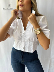 Mujer usando una blusa blanca con mangas cortas y botones elegantes, ideal para un look sofisticado y moderno. Perfecta para cualquier ocasión. Disponible en KIKE RODRIGUEZ.