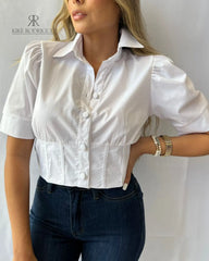 Mujer usando una blusa blanca con mangas cortas y botones elegantes, ideal para un look sofisticado y moderno. Perfecta para cualquier ocasión. Disponible en KIKE RODRIGUEZ.
