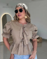 Mujer vistiendo la Blusa Sofía Nude de Kike Rodriguez con diseño peplum, lazos frontales y mangas tres cuartos, ideal para un look casual y elegante