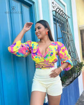 Mujer luciendo una vibrante blusa multicolor con escote en V y mangas abullonadas, perfecta para un look llamativo y moderno. Disponible en KIKE RODRIGUEZ.