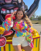 Mujer luciendo una blusa multicolor de hombros descubiertos y mangas largas, ideal para un look vibrante y colorido. Disponible en KIKE RODRIGUEZ.
