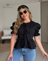 Mujer vistiendo la Blusa Matilda negra con diseño peplum, mangas abullonadas y lazos frontales, combinada con jeans para un look casual y moderno
