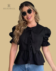 Mujer vistiendo la Blusa Matilda negra con diseño peplum, mangas abullonadas y lazos frontales, combinada con jeans para un look casual y moderno