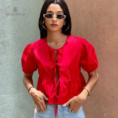 Mujer vistiendo la Blusa Matilda Roja con diseño peplum, mangas abullonadas y lazos frontales, combinada con jeans para un look casual y moderno
