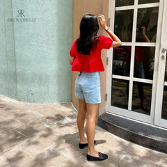 Mujer vistiendo la Blusa Matilda Roja con diseño peplum, mangas abullonadas y lazos frontales, combinada con jeans para un look casual y moderno