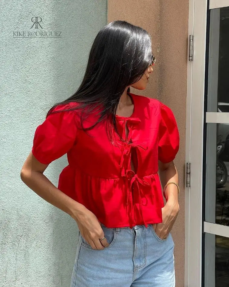 Mujer vistiendo la Blusa Matilda Roja con diseño peplum, mangas abullonadas y lazos frontales, combinada con jeans para un look casual y moderno