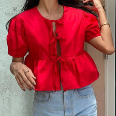 Mujer vistiendo la Blusa Matilda Roja con diseño peplum, mangas abullonadas y lazos frontales, combinada con jeans para un look casual y moderno