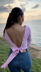 Mujer con blusa rosa con espalda descubierta disfrutando de una vista panorámica. Blusa ideal para un look casual y sofisticado. Disponible en KIKE RODRIGUEZ.