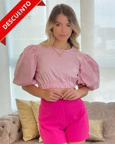Mujer vistiendo una blusa rosa con mangas abullonadas en descuento, ideal para un look moderno y sofisticado. Disponible en KIKE RODRIGUEZ.