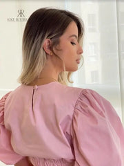 Mujer vistiendo una blusa rosa con mangas abullonadas en descuento, ideal para un look moderno y sofisticado. Disponible en KIKE RODRIGUEZ.