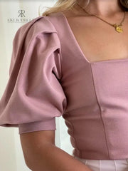 Mujer con una blusa rosa de mangas abullonadas en descuento, mostrando un estilo sofisticado y elegante, perfecta para cualquier ocasión.