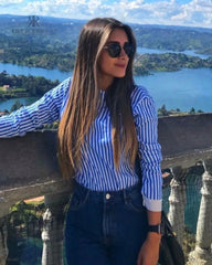 Mujer con blusa de rayas con espalda descubierta disfrutando de una vista panorámica. Blusa perfecta para un look casual y sofisticado. Disponible en KIKE RODRIGUEZ.