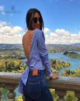 Mujer con blusa de rayas con espalda descubierta disfrutando de una vista panorámica. Blusa perfecta para un look casual y sofisticado. Disponible en KIKE RODRIGUEZ.