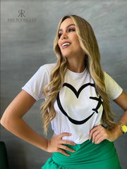 Camiseta blanca con diseño de corazón y avión en promoción especial de 3 por $129,900, disponible en KIKE RODRIGUEZ. Ideal para los amantes de los viajes y la moda.