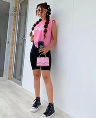 Modelo luciendo una camiseta rosa Barbie con estilo casual y moderno, combinada con leggings negros y accesorios a la moda, ideal para un look relajado y chic.