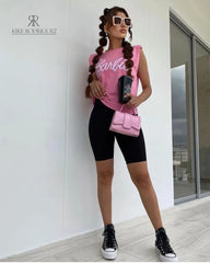 Modelo luciendo una camiseta rosa Barbie con estilo casual y moderno, combinada con leggings negros y accesorios a la moda, ideal para un look relajado y chic.