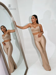 Mujer vistiendo un conjunto dorado sexy de KIKE RODRIGUEZ, compuesto por un top ajustado y pantalones acampanados, posando frente a un espejo para resaltar su figura.