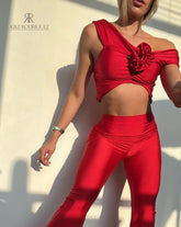 Mujer vistiendo un conjunto rojo sexy de KIKE RODRIGUEZ, con un top off-shoulder y pantalones acampanados, mostrando un look elegante y atractivo bajo la luz del sol.