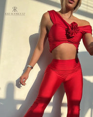 Mujer vistiendo un conjunto rojo sexy de KIKE RODRIGUEZ, con un top off-shoulder y pantalones acampanados, mostrando un look elegante y atractivo bajo la luz del sol.