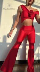 Mujer vistiendo un conjunto rojo sexy de KIKE RODRIGUEZ, con un top off-shoulder y pantalones acampanados, mostrando un look elegante y atractivo bajo la luz del sol.