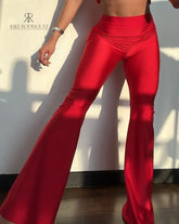 Mujer vistiendo un conjunto rojo sexy de KIKE RODRIGUEZ, con un top off-shoulder y pantalones acampanados, mostrando un look elegante y atractivo bajo la luz del sol.