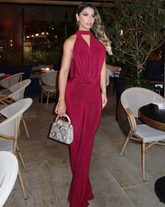 Mujer luciendo el Enterizo Eclipse VinoTinto con escote halter y espalda descubierta, sosteniendo bolso blanco, en ambiente elegante.