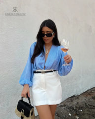 Falda blanca elegante con cinturón negro, combinada con una blusa de rayas azules y una cartera negra.