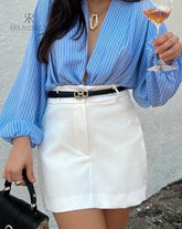 Falda blanca elegante con cinturón negro, combinada con una blusa de rayas azules y una cartera negra.