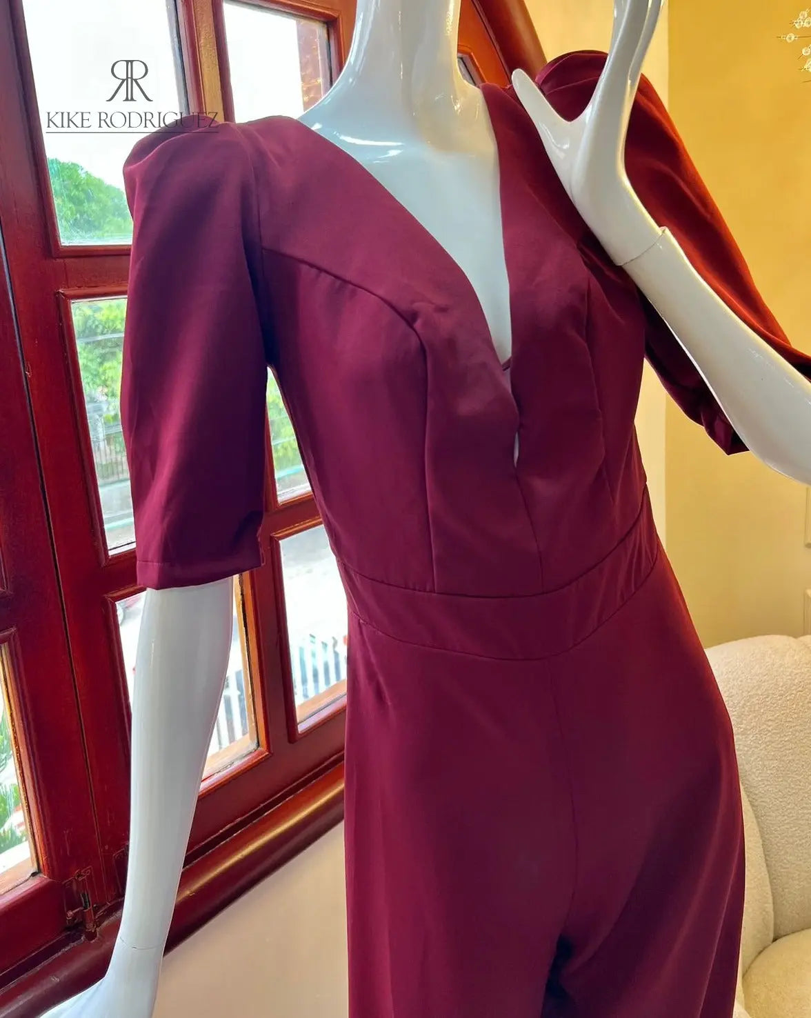 Maniquí luciendo un elegante mono vinotinto con mangas abullonadas, una prenda perfecta para eventos especiales y ocasiones formales de KIKE RODRIGUEZ.