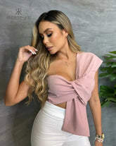 Mujer con top asimétrico rosa con lazo frontal, ideal para ocasiones especiales con un estilo elegante y sofisticado.