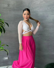 Mujer luciendo un top blanco con mangas de malla y detalles cruzados, combinado con una falda rosa, ideal para un look moderno y elegante.