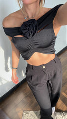 Mujer luciendo un top negro asimétrico con detalle de flor, perfecto para un look sofisticado y moderno. Disponible en KIKE RODRIGUEZ.