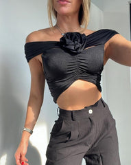Mujer luciendo un top negro asimétrico con detalle de flor, perfecto para un look sofisticado y moderno. Disponible en KIKE RODRIGUEZ.