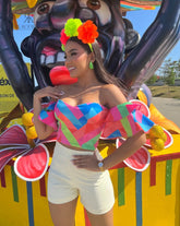Mujer vistiendo un top de hombros descubiertos con un vibrante diseño colorido, ideal para destacar en eventos. Disponible en KIKE RODRIGUEZ.