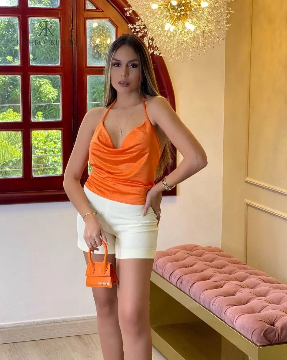 Mujer luciendo un elegante top de tirantes en seda naranja de KIKE RODRIGUEZ, ideal para ocasiones especiales y combinable con shorts blancos.