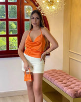 Mujer luciendo un elegante top de tirantes en seda naranja de KIKE RODRIGUEZ, ideal para ocasiones especiales y combinable con shorts blancos.