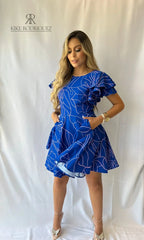 Mujer con un vestido azul rey con volantes y bolsillos de KIKE RODRIGUEZ, perfecto para cualquier ocasión y evento elegante.