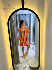 Mujer posando frente al espejo con un vestido a rayas en tonos naranja y volantes en el dobladillo, perfecto para el verano y ocasiones casuales.