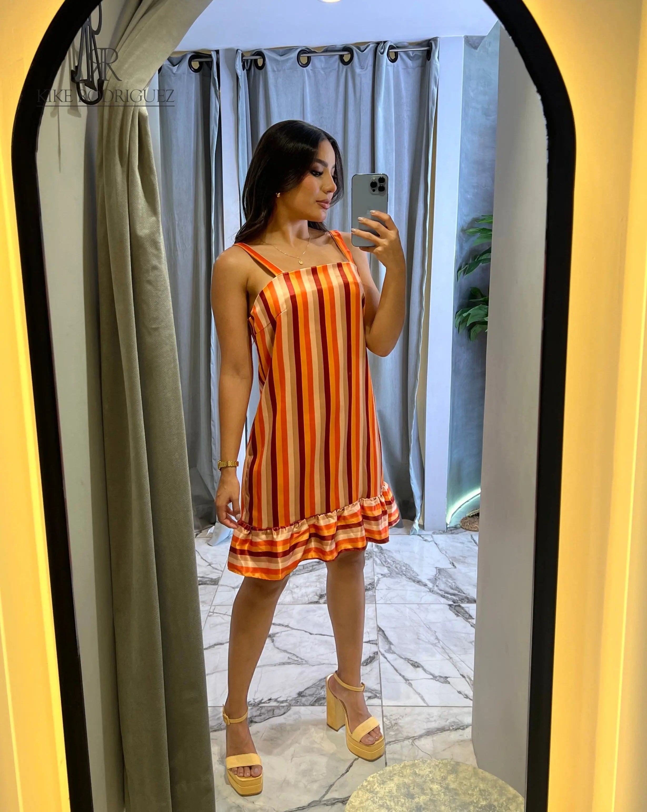 Mujer posando frente al espejo con un vestido a rayas en tonos naranja y volantes en el dobladillo, perfecto para el verano y ocasiones casuales.