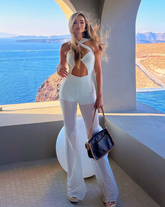 Mujer usando enterizo blanco cruzado con cut-out frontal y pantalón bota ancha junto a piscina iluminada – KIKE RODRIGUEZ.