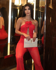 Mujer usando enterizo rojo con escote profundo y flores 3D, pantalón elegante y clutch blanco – KIKE RODRIGUEZ.