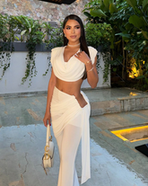 Mujer luciendo el Set Atenea Blanco, top drapeado y pantalón elegante, en ambiente exterior sofisticado.