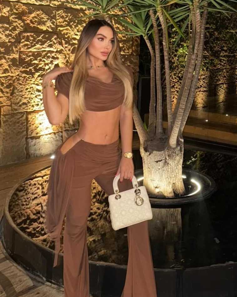 Mujer luciendo el Set Atenea Mocca, top drapeado y pantalón elegante, en ambiente nocturno sofisticado.