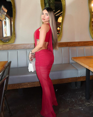 Mujer luciendo el Set Taurus ROJO en tono rojo, de espalda, en un ambiente moderno con paredes de piedra y muebles blancos. Vestido ajustado con diseño asimétrico y apertura lateral.