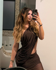 Mujer posando frente al espejo con el Set Taurus MOCCA, vestido marrón con corte lateral y escote asimétrico, peinado con ondas y maquillaje natural.