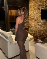 Mujer sentada en sofá blanco usando el Set Taurus MOCCA, conjunto ajustado en tono mocca con abertura lateral, en sala elegante con pared de piedra y mesa de madera.