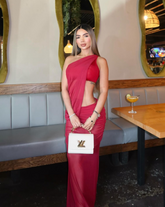 Mujer luciendo el Set Taurus ROJO en tono rojo, de espalda, en un ambiente moderno con paredes de piedra y muebles blancos. Vestido ajustado con diseño asimétrico y apertura lateral.