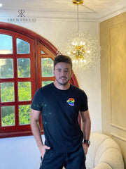 Camiseta negra con un pequeño estampado de arcoíris en el pecho. Perfecta para un look casual y elegante. Disponible en promoción de 3 por $129,900 en KIKE RODRIGUEZ. Ideal para mostrar apoyo a la diversidad.